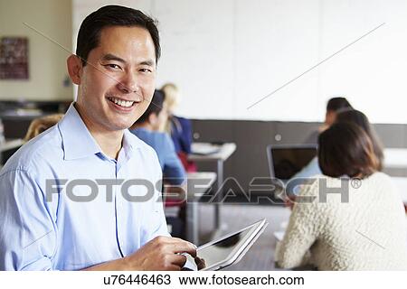 Stock Image - High School Teacher With Digital Tablet In Classroom. Fotosearch