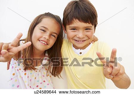 Picture - Hispanic Boy And Girl Standing By Wall Making Peace Sign. Fotosearch