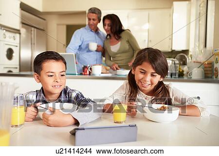 Picture - Hispanic Family Eating Breakfast Using Digital Devices. Fotosearch