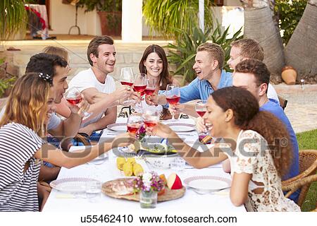 Stock Image - Large Group Of Young Friends Enjoying Outdoor Meal Together. Fotosearch