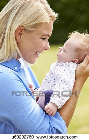 Stock Image - Loving Mother Holding Baby Daughter In Garden. Fotosearch