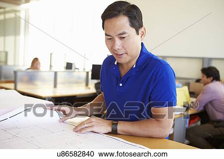 Stock Image - Male Architect Studying Plans In Office. Fotosearch
