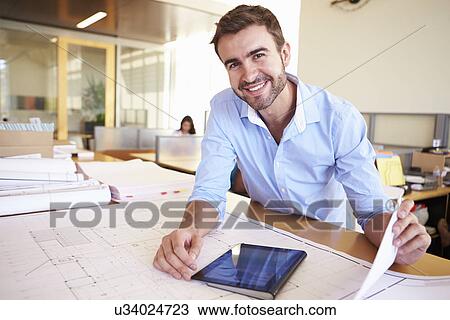 Stock Image - Male Architect With Digital Tablet Studying Plans In Office. Fotosearch