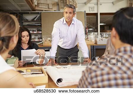 Stock Image - Male Boss Leading Meeting Of Architects Sitting At Table. Fotosearch