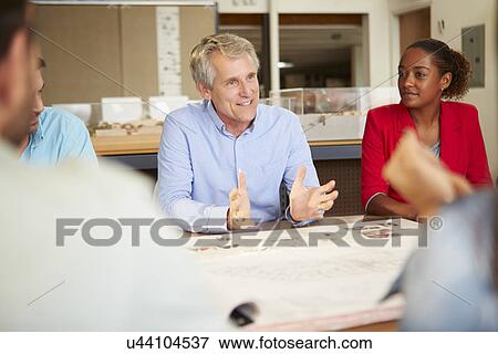 Stock Photo - Male Boss Leading Meeting Of Architects Sitting At Table. Fotosearch