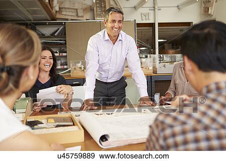 Stock Photo - Male Boss Leading Meeting Of Architects Sitting At Table. Fotosearch