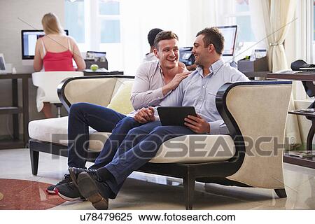 Male Couple Sitting In Hotel Lobby Looking At Digital Tablet View Large Photo Image Stock Photography - Male Couple Sitting In Hotel Lobby Looking At Digital Tablet. Fotosearch