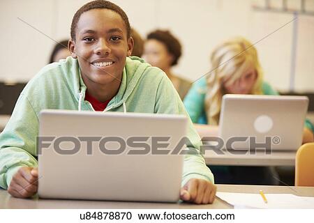 Stock Image - Male High School Student At Desk In Class Using Laptop. Fotosearch