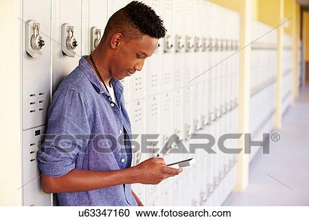Stock Image - Male High School Student By Lockers Using Mobile Phone. Fotosearch