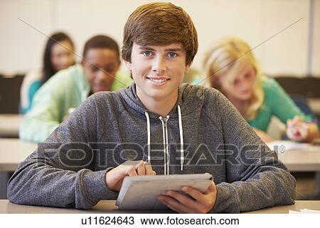 Stock Image - Male High School Student Studying At Desk In Classroom. Fotosearch