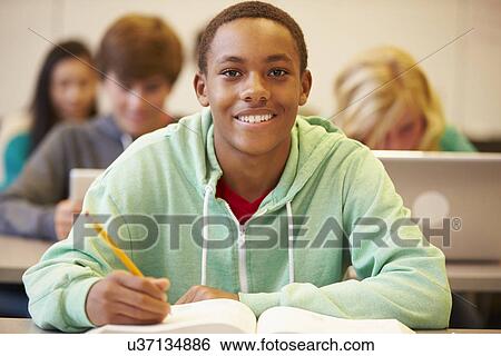 Stock Photograph - Male High School Student Studying At Desk In Classroom. Fotosearch