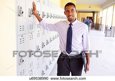 Stock Image - Male High School Teacher Standing By Lockers. Fotosearch