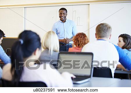 Stock Image - Male Tutor Teaching University Students In Classroom. Fotosearch