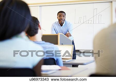 Stock Image - Male Tutor Teaching University Students In Classroom. Fotosearch
