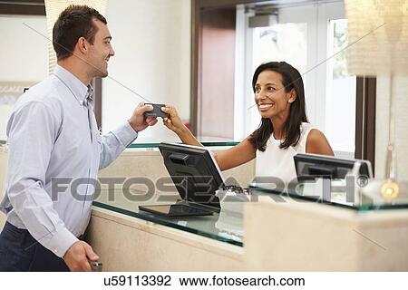 Stock Image - Man Checking In At Hotel Reception. Fotosearch