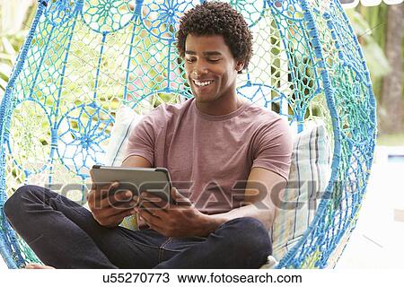 Stock Image - Man On Outdoor Garden Swing Seat Using Digital Tablet. Fotosearch
