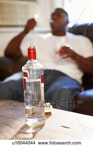 Picture - Man Sitting On Sofa With Bottle Of Vodka And Cigarettes. Fotosearch