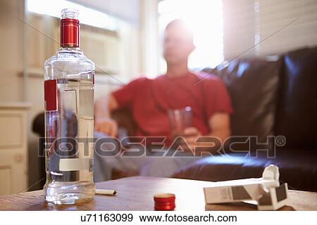 Stock Photo - Man Sitting On Sofa With Bottle Of Vodka And Cigarettes. Fotosearch