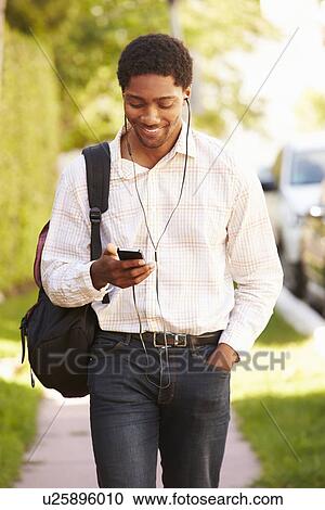 Stock Image - Man Walking Along Street To Work Listening To Music. Fotosearch