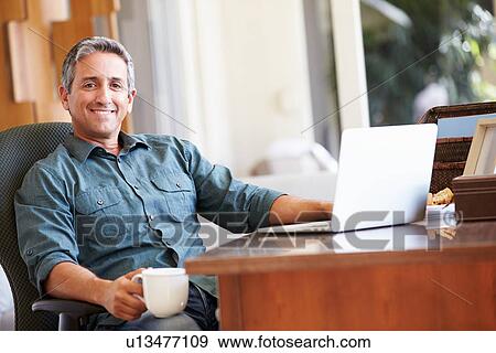 Stock Photo - Mature Hispanic Man Using Laptop On Desk At Home. Fotosearch
