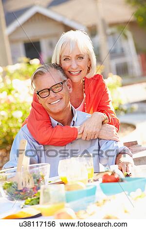 Stock Photograph - Mature Romantic Couple Enjoying Outdoor Meal In Garden. Fotosearch