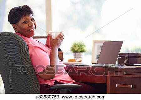 Stock Photo - Mature Woman Using Laptop On Desk At Home. Fotosearch