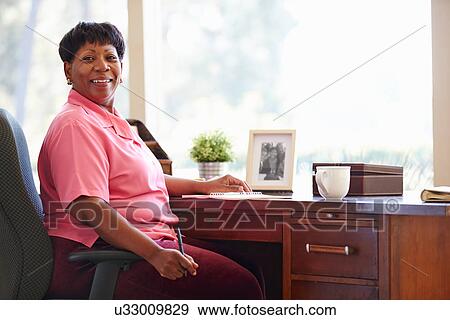 Mature Woman Writing In Notebook Sitting At Desk View Large Photo Image Stock Photo - Mature Woman Writing In Notebook Sitting At Desk. Fotosearch