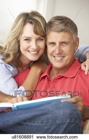 Stock Image - Mid age couple reading book together. Fotosearch