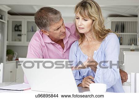 Picture - Mid age couple working at home on laptop. Fotosearch