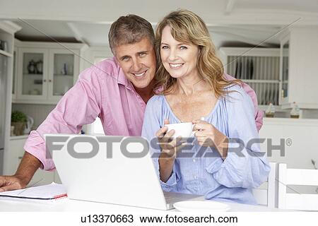 Mid age couple working at home on laptop View Large Photo Image Stock Image - Mid age couple working at home on laptop. Fotosearch
