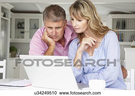 Mid age couple working at home on laptop View Large Photo Image Stock Image - Mid age couple working at home on laptop. Fotosearch