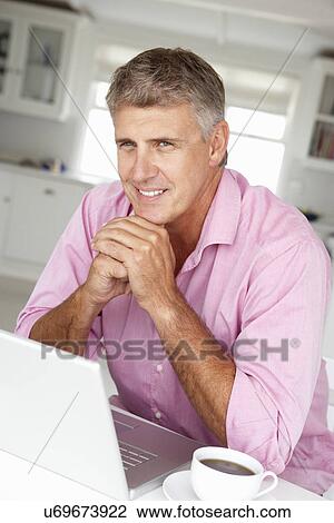 Stock Image - Mid age man working on laptop at home. Fotosearch