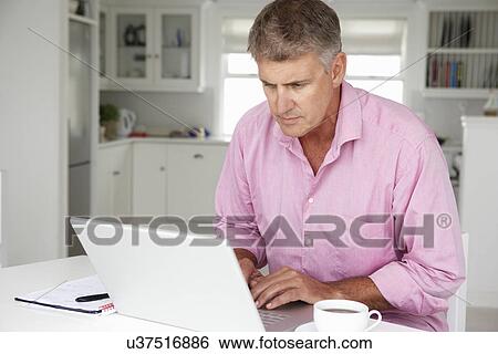Mid age man working on laptop at home View Large Photo Image Stock Photograph - Mid age man working on laptop at home. Fotosearch