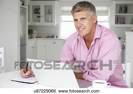 Stock Photograph - Mid age man working on laptop at home. Fotosearch