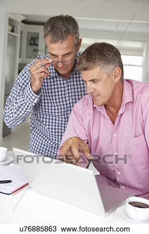Stock Image - Mid age men working on laptop at home. Fotosearch
