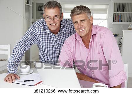 Stock Photograph - Mid age men working on laptop at home. Fotosearch