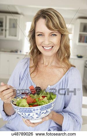 Stock Photograph - Mid age woman eating salad. Fotosearch
