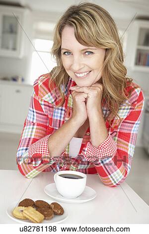 Stock Photo - Mid age woman with coffee and biscuits at home. Fotosearch