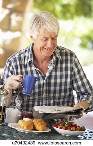 Stock Photo - Middle aged man eating breakfast outdoors. Fotosearch
