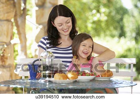 Stock Image - Mother and daughter eating breakfast outdoors. Fotosearch
