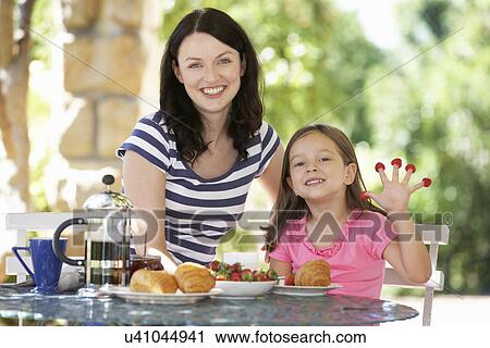 Stock Image - Mother and daughter eating breakfast outdoors. Fotosearch