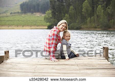 Mother and daughter sitting on a jetty View Large Photo Image Stock Image - Mother and daughter sitting on a jetty. Fotosearch