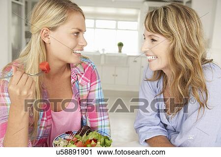 Stock Image - Mother and teenage daughter enjoying food at home. Fotosearch