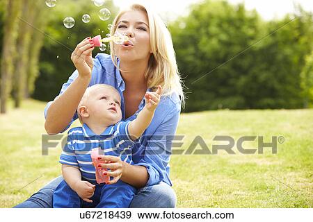 Stock Photo - Mother Blowing Bubbles For Young Boy In Garden. Fotosearch