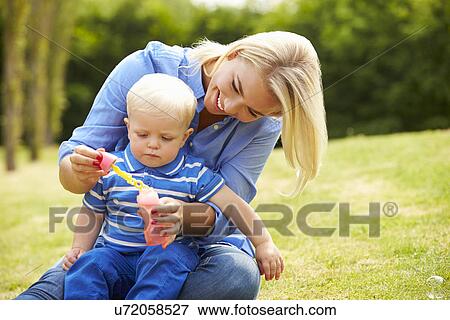 Stock Photo - Mother Blowing Bubbles For Young Boy In Garden. Fotosearch