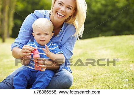 Stock Photo - Mother Blowing Bubbles For Young Boy In Garden. Fotosearch