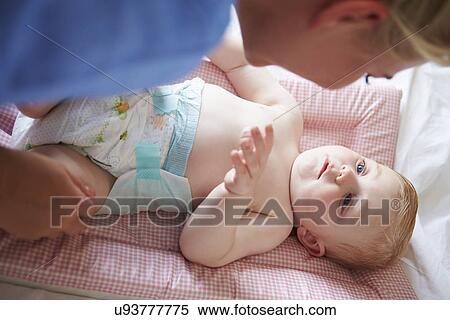 Stock Photography - Mother Changing Baby Son's Nappy As He Lies On Mat. Fotosearch