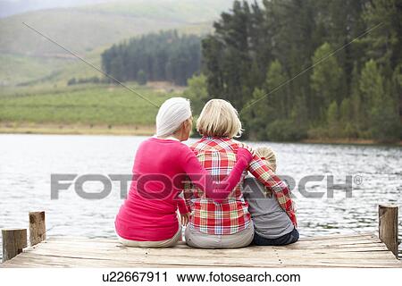 Stock Image - Mother, daughter and grandmother sitting on a jetty. Fotosearch