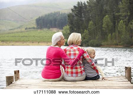 Stock Photo - Mother, daughter and grandmother sitting on a jetty. Fotosearch