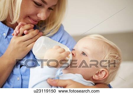 Stock Image - Mother Giving Baby Son Bottle Of Milk. Fotosearch
